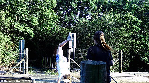Children are seen doing handstands and playing chicken with high speed trains – forcing busy level crossing to close