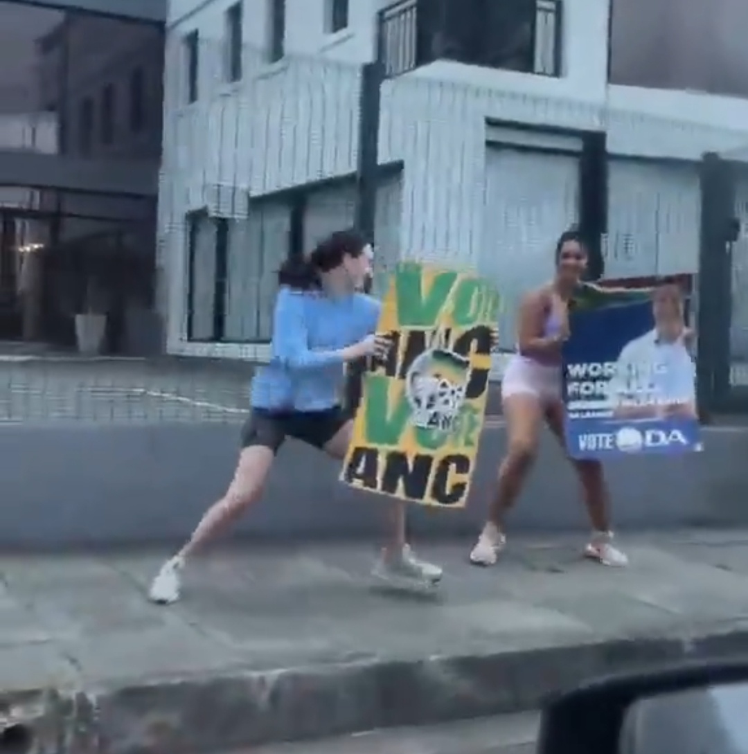 Two white women hold ANC and DA placards for passing motorists in a CBD