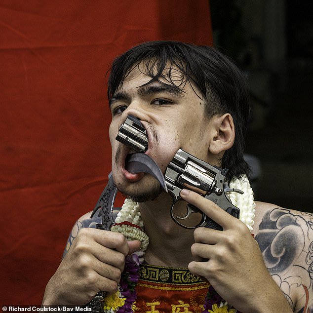 Feeling lucky, monk? Devotee shoves a handgun through his cheek as worshippers show devotion at Thai festival