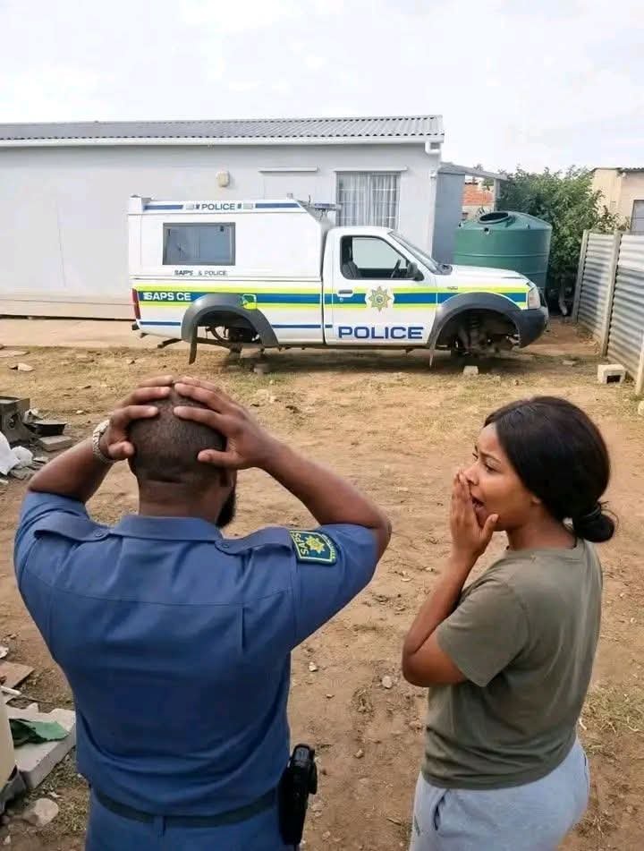 Image shows an SAPS bakkie with no wheels as two officers stand beside it