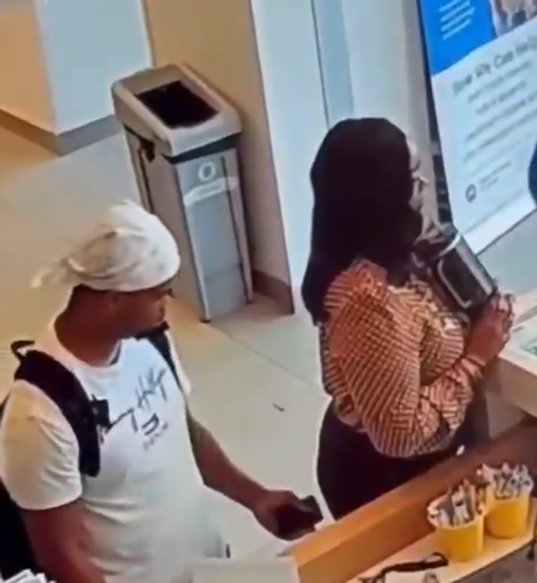Man appears to stick his tongue out at a woman from behind at a reception desk